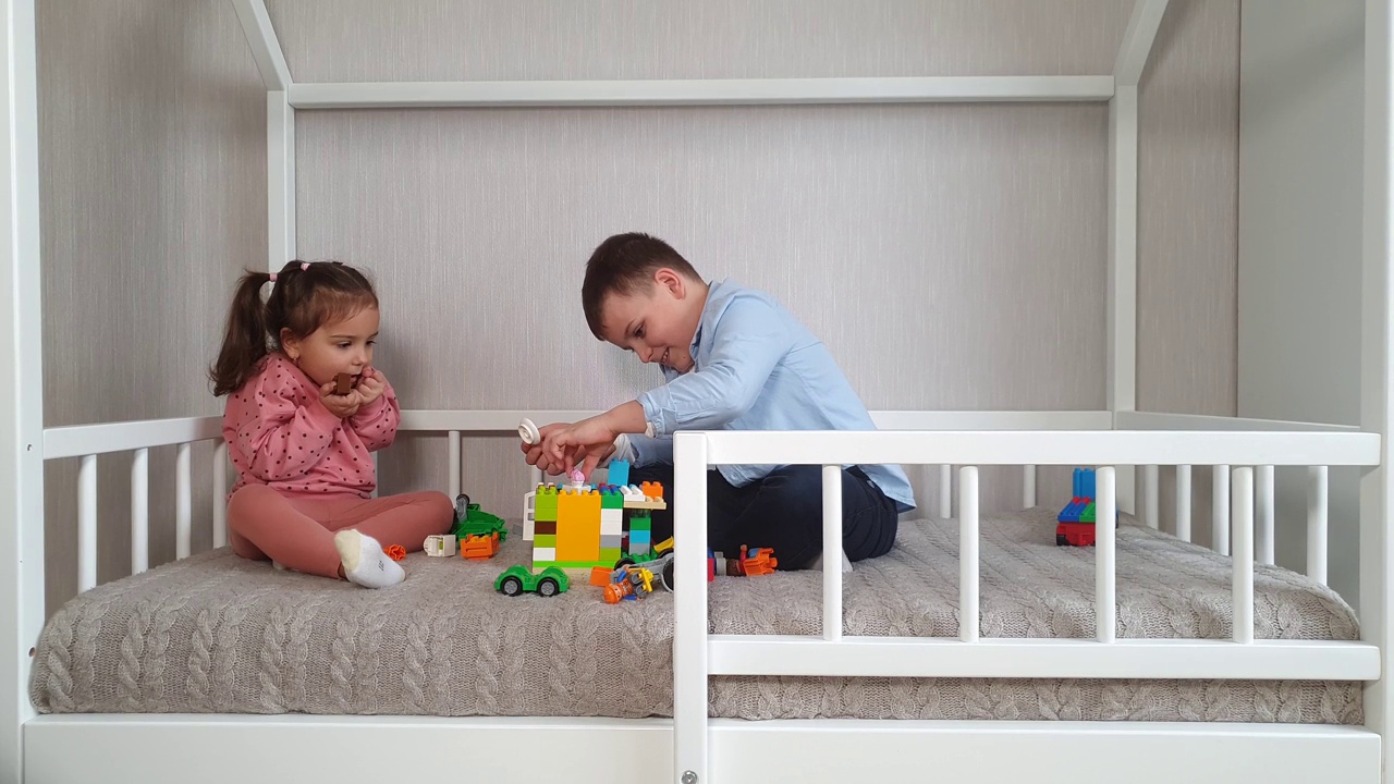 两个孩子兄妹正坐在一张蒙台梭利床上，玩着积木方块。视频下载