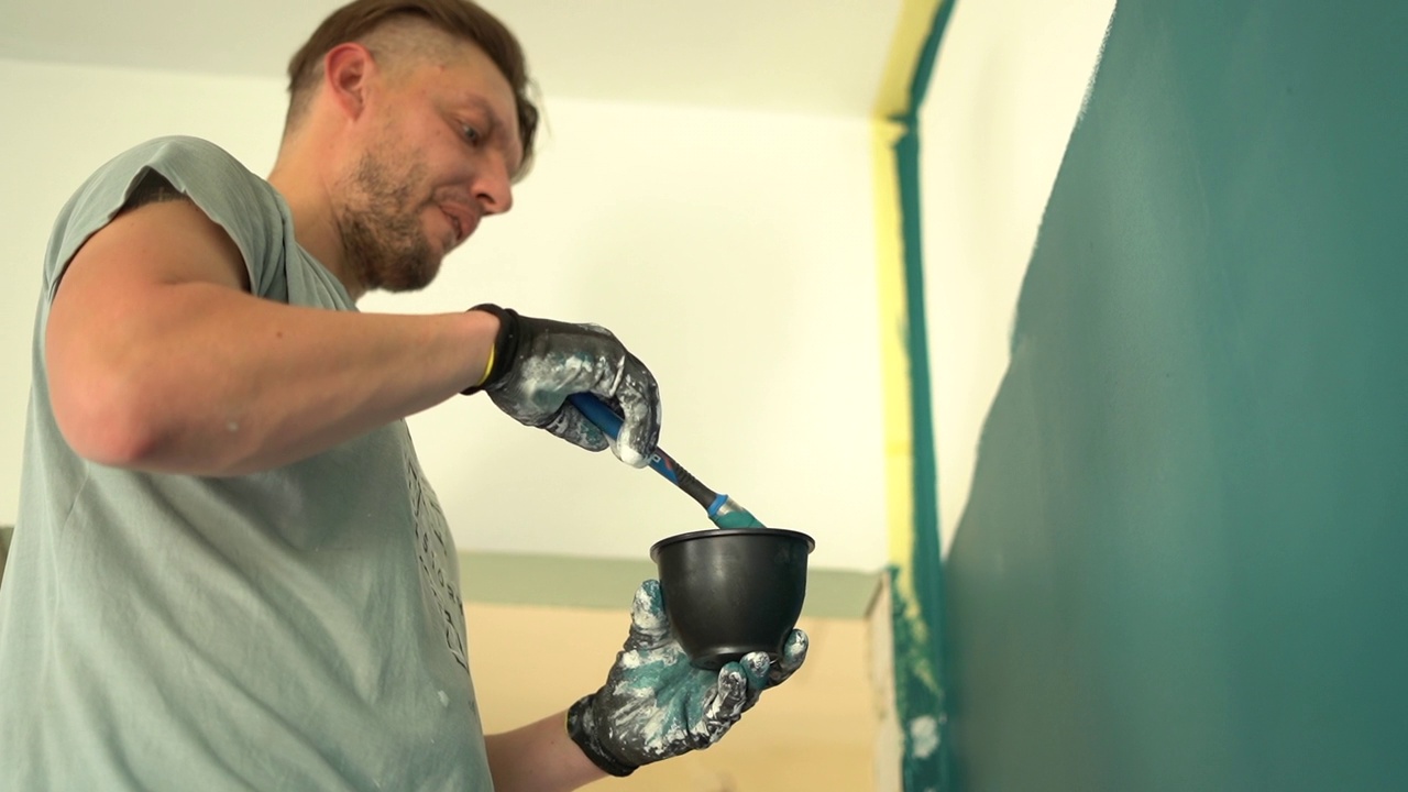 成熟的男性工人用刷子搅拌油漆，站在梯子上刷墙，进行修理和装修概念视频下载
