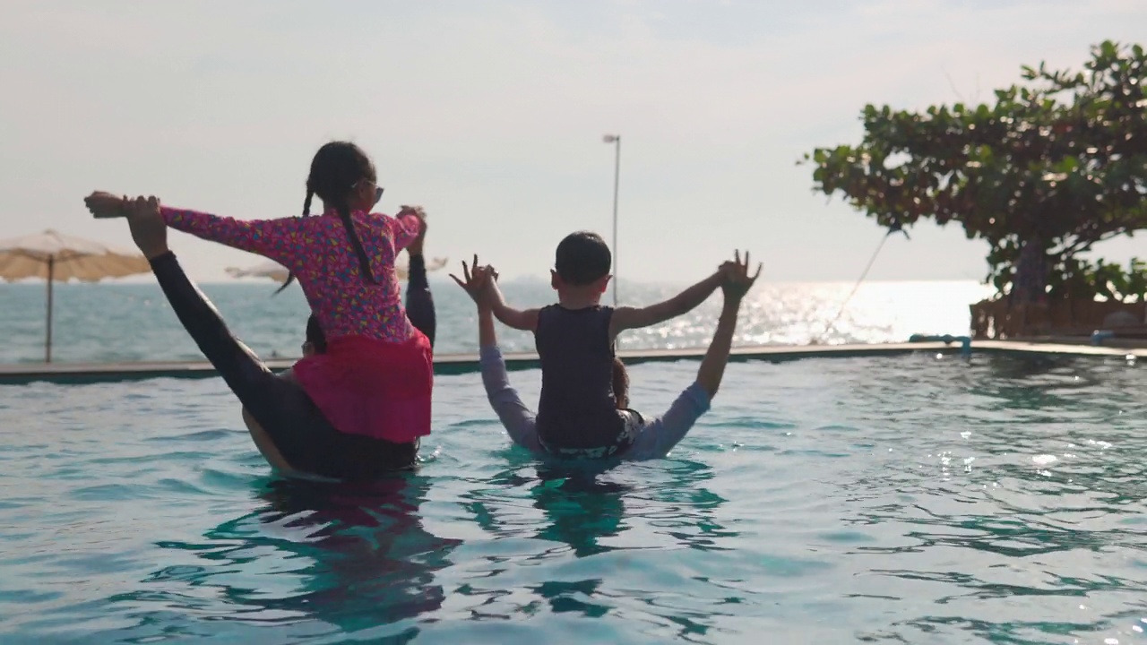 幸福的亚洲家庭:亚洲男孩和女孩骑在爸爸妈妈的脖子上，一起玩进游泳池视频素材