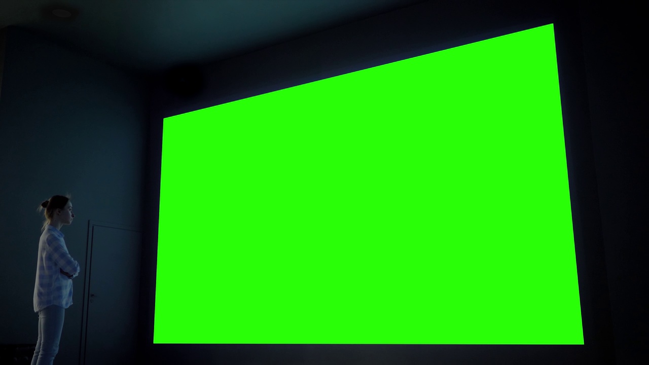 女人看着大空白绿色屏幕在黑暗的房间-色度键概念视频下载