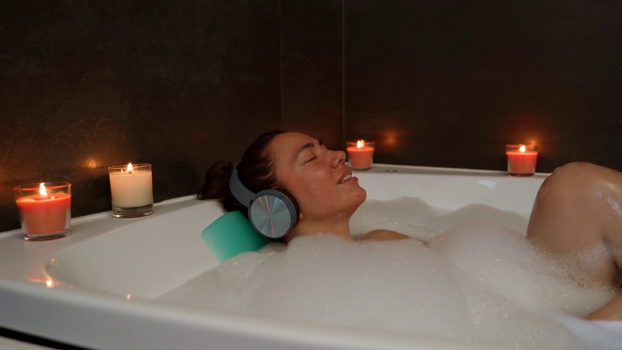 浴缸里戴着耳机的冷静女人视频素材