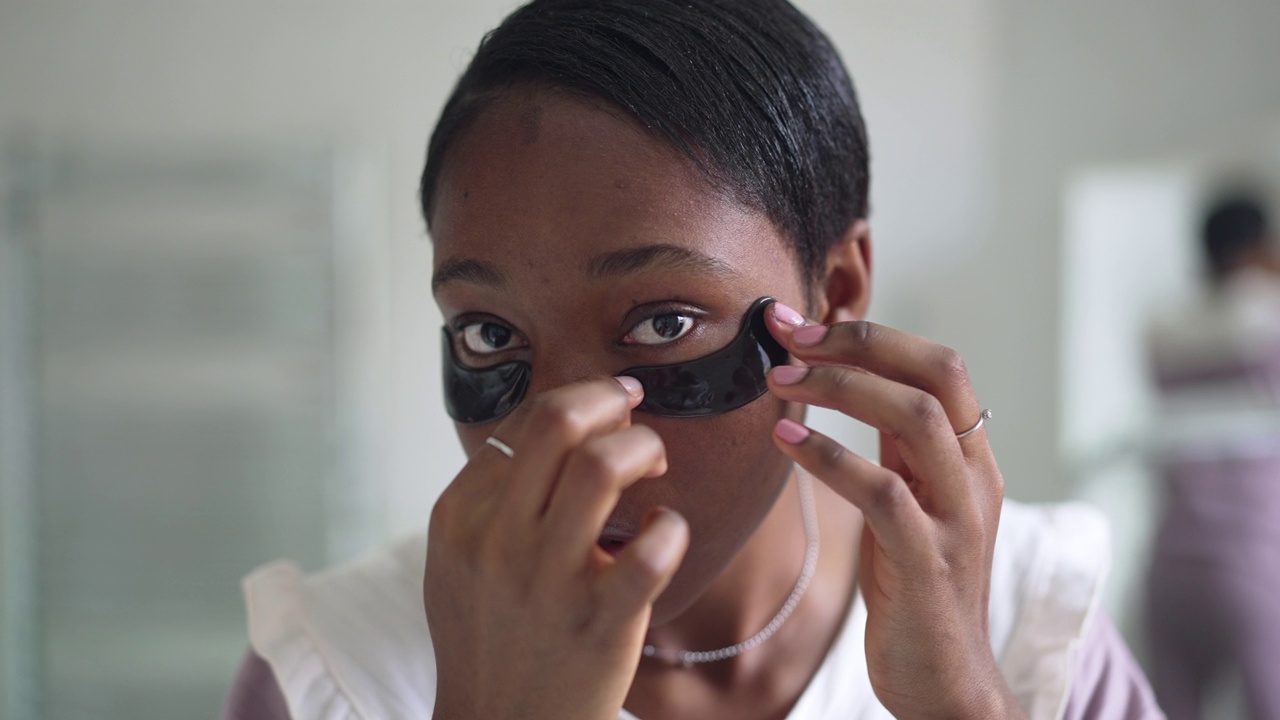 年轻的非洲裔美国妇女的特写脸，用慢镜头看着镜头，戴着眼罩。前视图肖像苗条美丽的女士照顾皮肤早上在浴室。视频素材