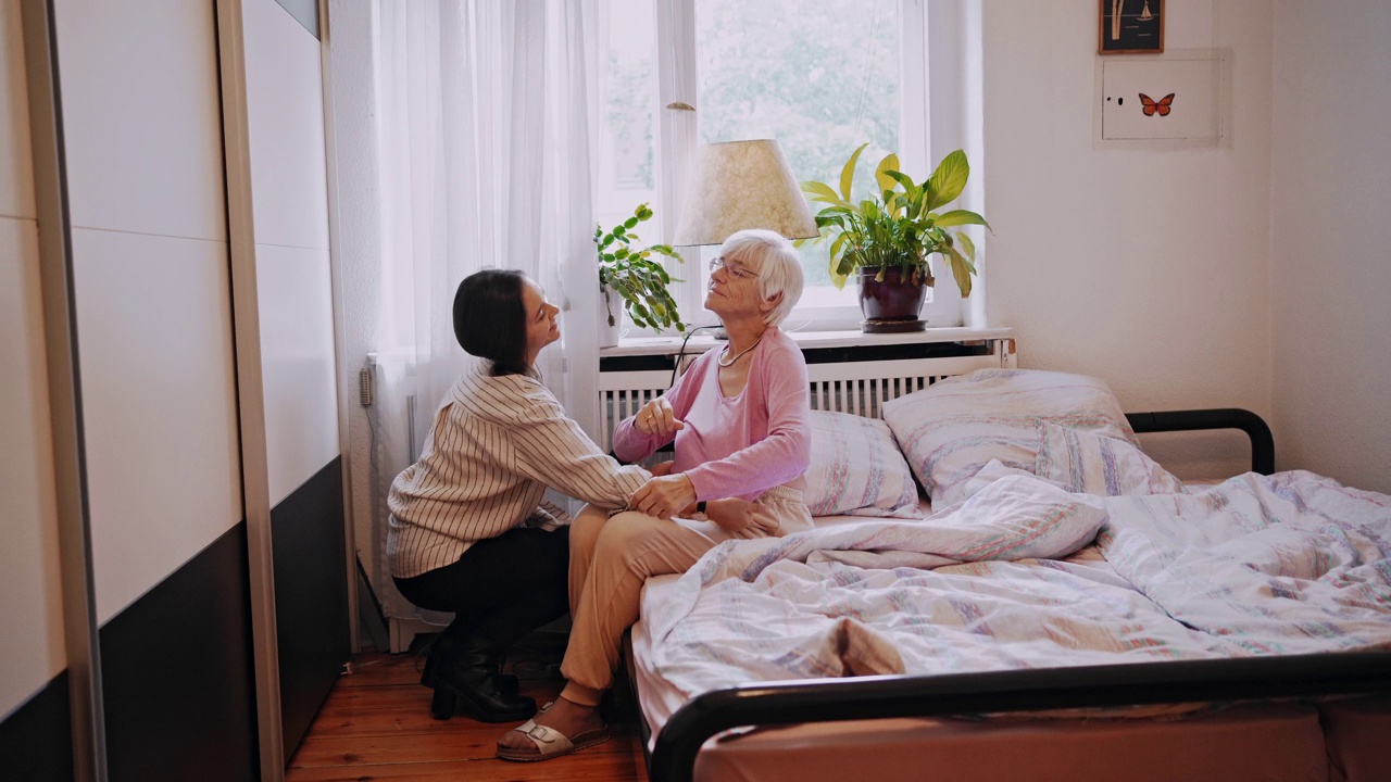 女保健工作者帮助老年妇女在卧室穿上衣视频素材