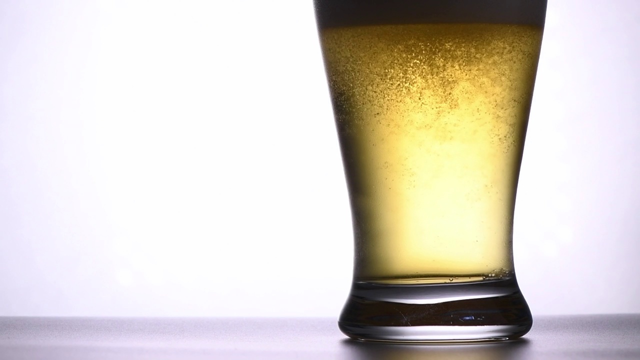 白色背景下，将新鲜的啤酒倒入玻璃中的慢镜头视频素材