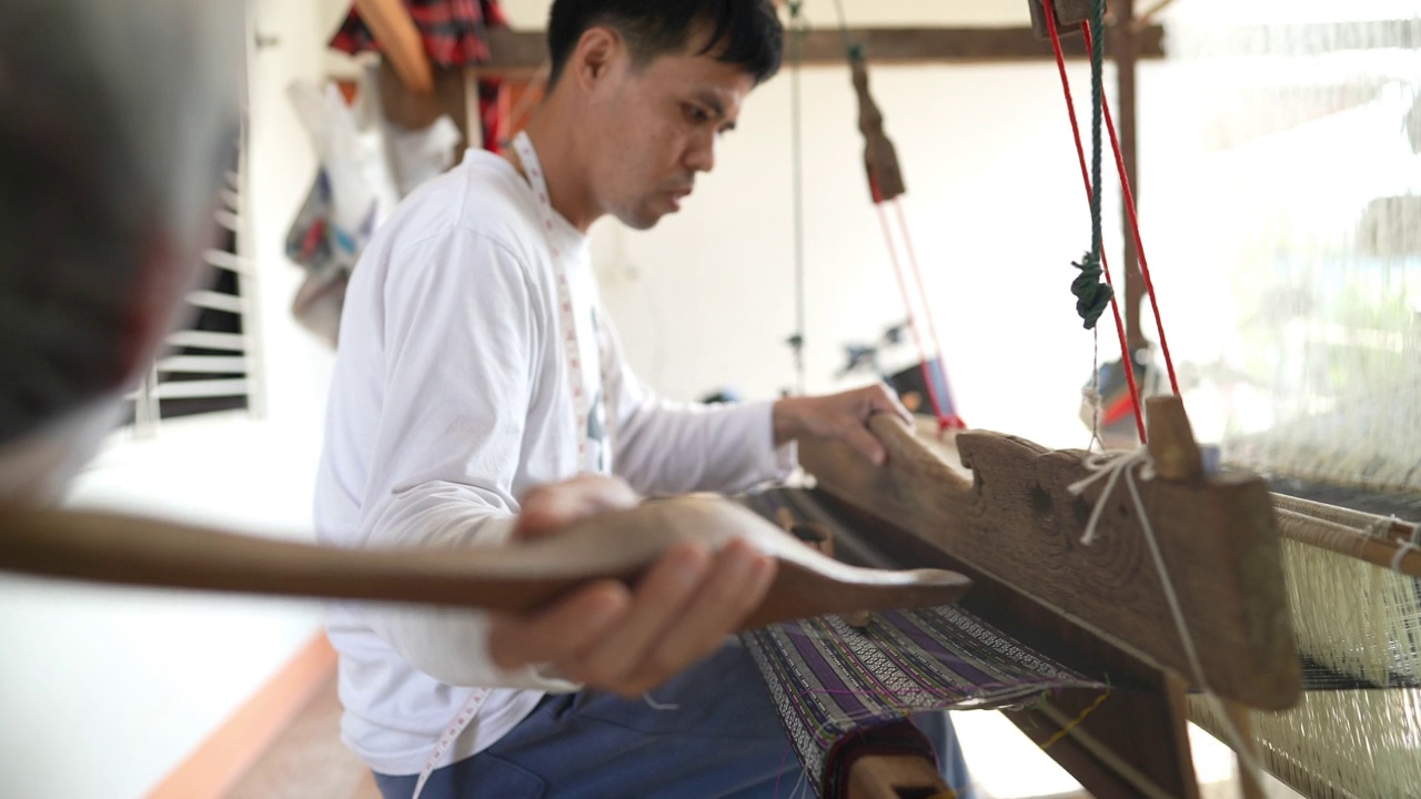 年轻的亚洲男子用传统的木制织布机织布。世代相传的日常生活可持续性视频下载