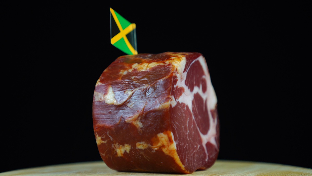 美味的烟熏里脊肉配牙买加小旗，黑色背景上的一块肉旋转着。视频下载
