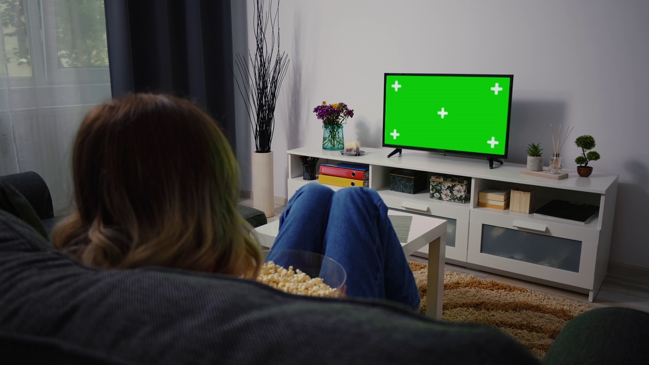 坐在家里的沙发上看绿色电视的女人视频下载