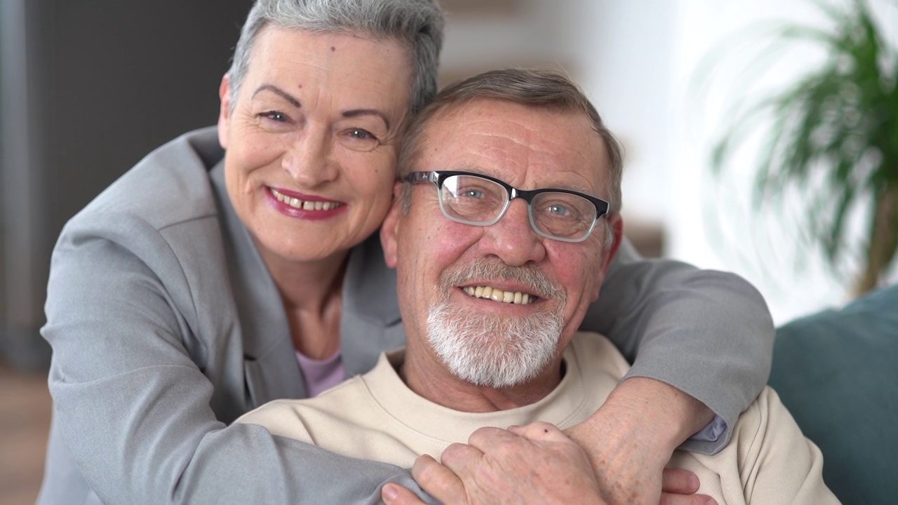一个男人和一个女人坐在沙发上拥抱着看着镜头。一对白发苍苍的老夫妇的印多尔肖像视频下载
