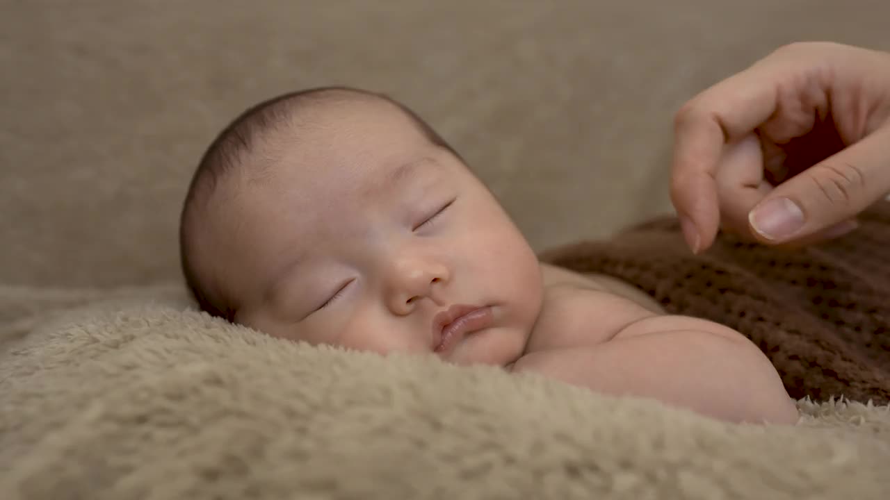4k，两个月大的亚洲新生儿的特写，睡在棕色的地毯上。有母亲的手握在脸颊上表达爱。视频素材