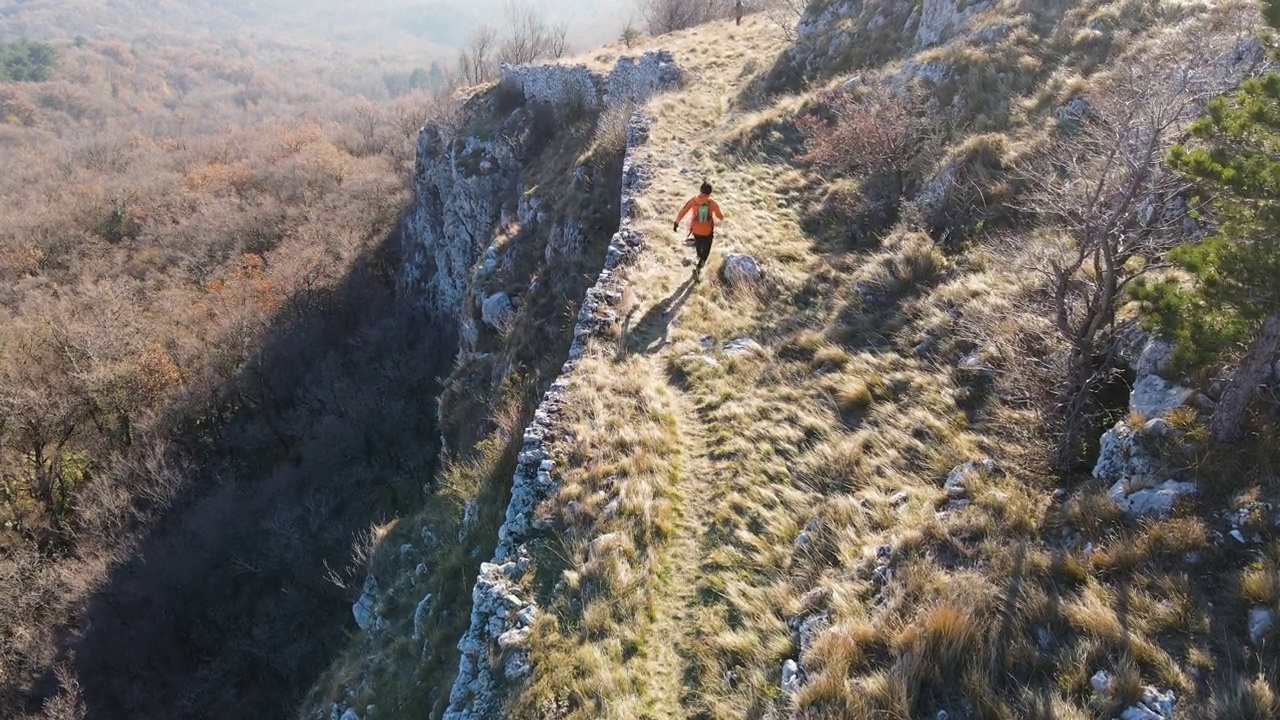 鸟瞰图，一个年轻人跑下山的悬崖在山上视频下载