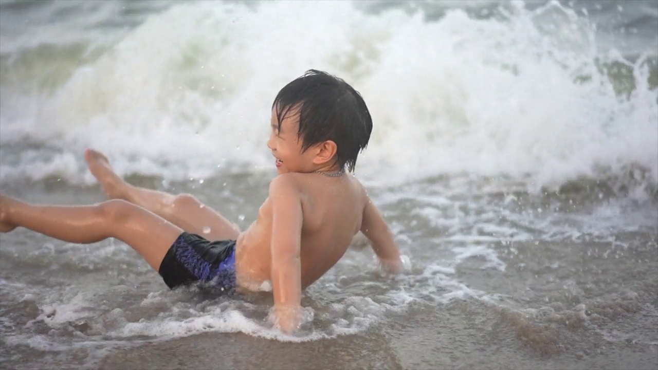 慢镜头拍摄的亚洲男孩在沙滩上享受和玩海和沙子视频下载