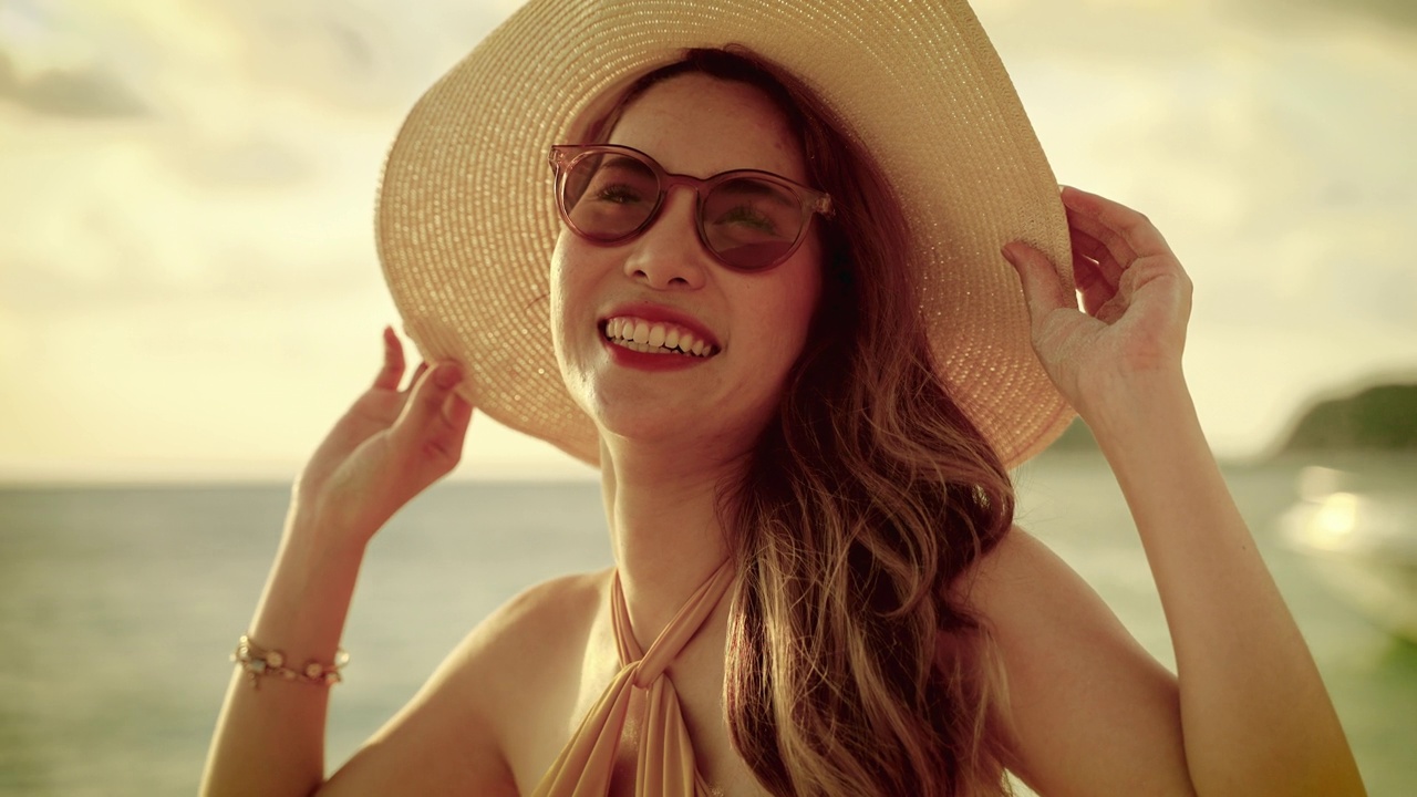 在傍晚的太阳是日落，美丽的亚洲女孩戴着墨西哥帽，走在沙滩上她的假期，自由的概念，旅行，冒险。视频下载