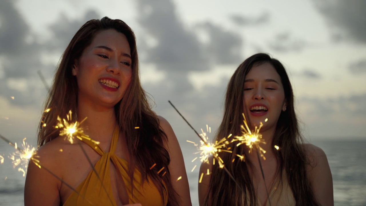 美丽的亚洲女人和她的朋友在海滩玩火花在暮光之城。视频素材