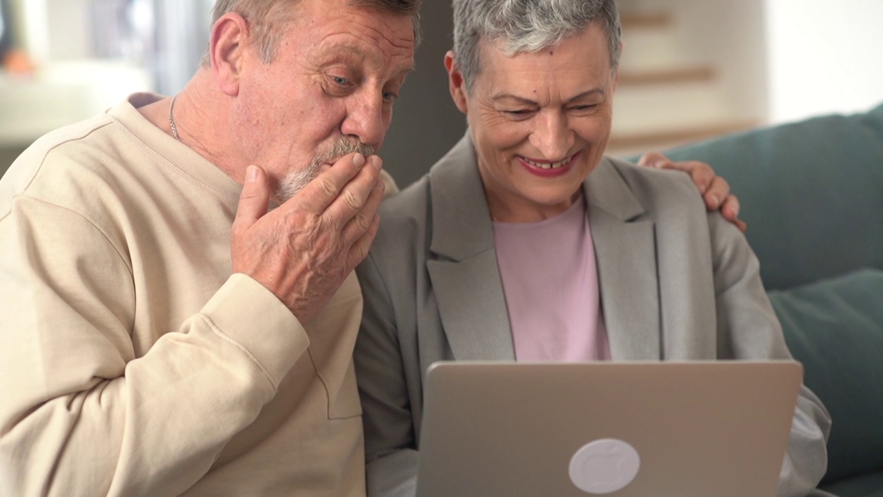 一对幸福的退休夫妇坐在沙发上互相拥抱，进行视频通话。丈夫和妻子与朋友视频通话视频下载