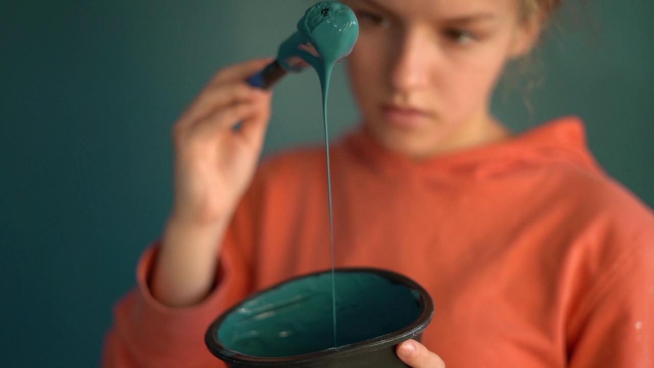 一个刷子和一碗蓝色颜料的特写，与一幅穿着橙色运动衫的十几岁女孩的肖像对比。一个女孩的画像视频下载