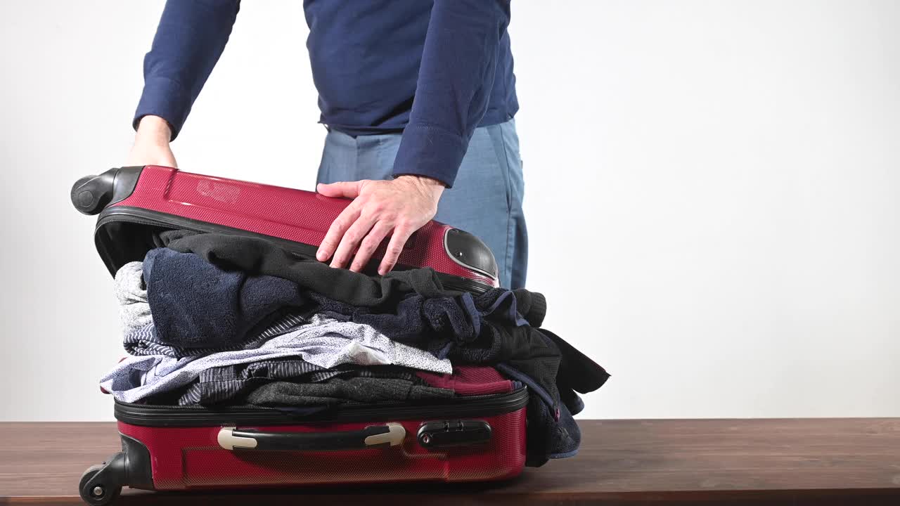 一个人(男人)在家里收拾行李去度假。他用腿压，但他做不到。事情太多了!视频下载