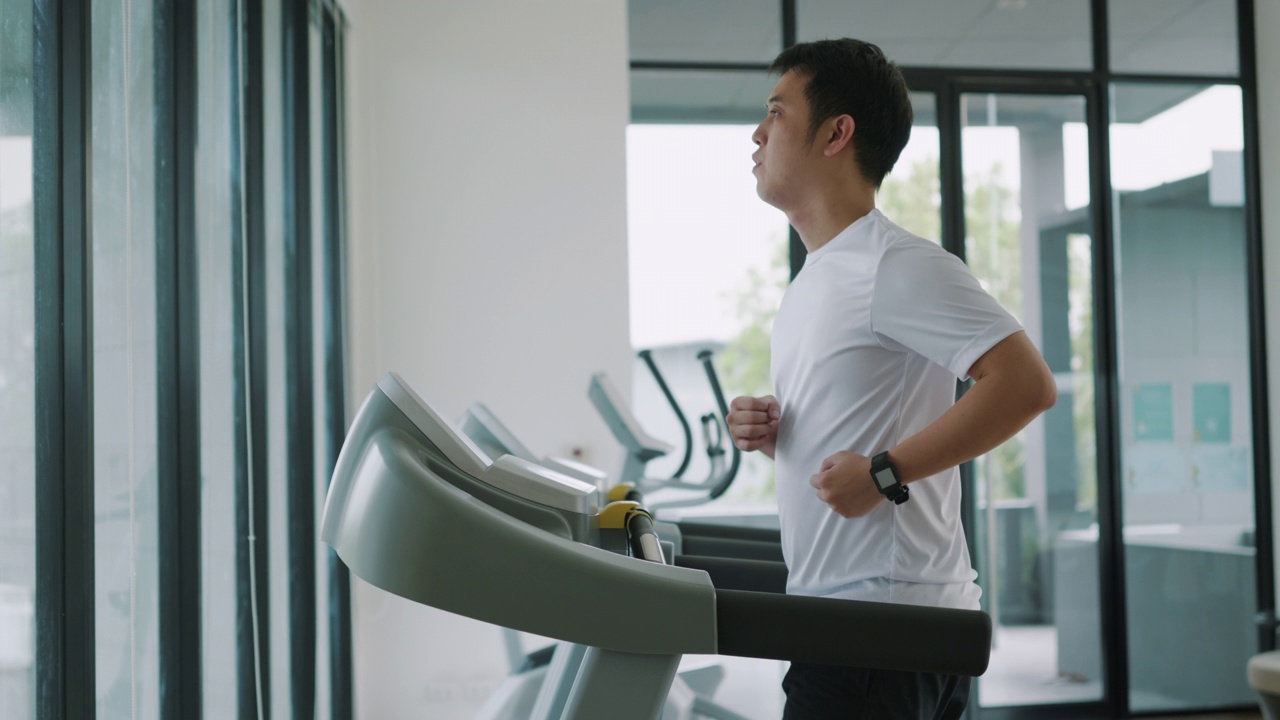 一个亚洲人在健身房的跑步机上跑步。视频下载