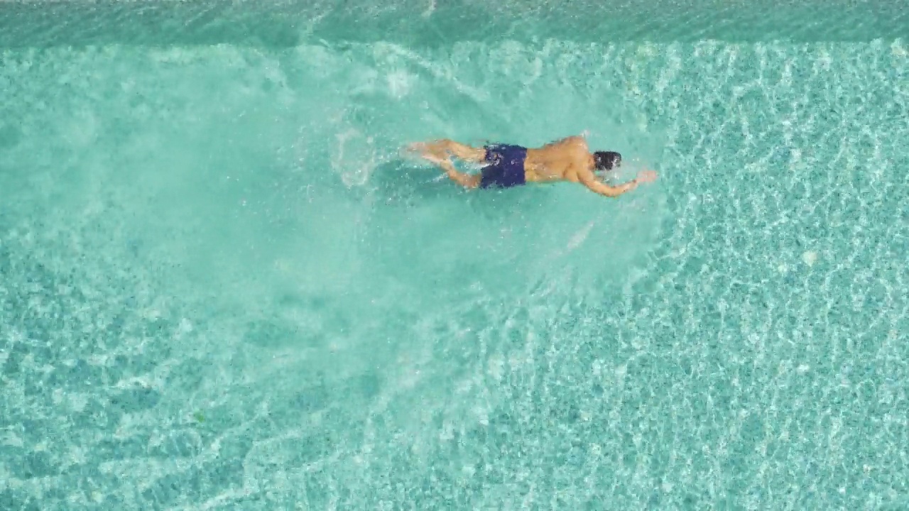 俯视一个人在蓝色或绿松石游泳池与清澈的水波纹在夏季游泳。人们度假时的生活方式。视频下载