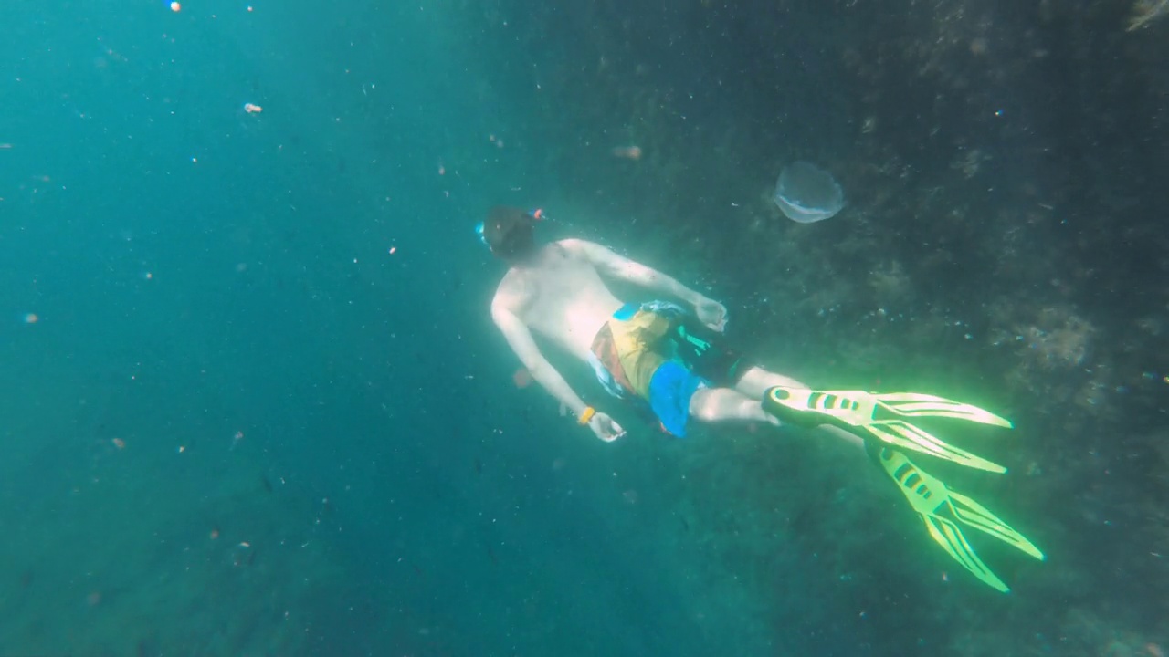 年轻的白人男子带着潜水面罩和脚蹼在水下自由潜水。用动作摄像机拍摄视频素材