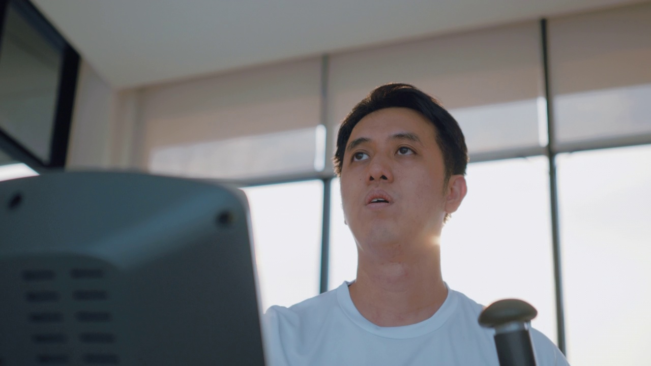 一个亚洲人在健身房里的椭圆机上跑步的中镜头。视频下载