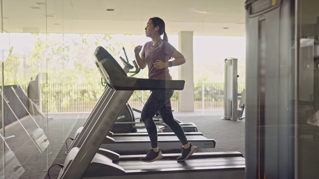 年轻女子在健身房的跑步机上锻炼视频下载