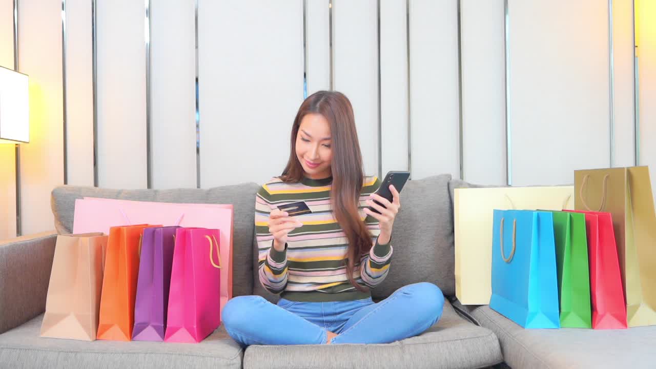 年轻亚洲女性使用手提电脑或手机及信用卡在网上购物视频下载
