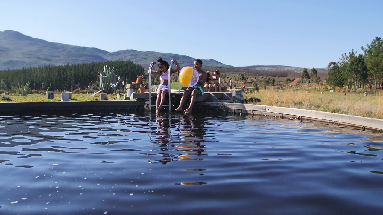 好玩的兄弟姐妹与沙滩球在阳光明媚的乡村游泳池视频下载