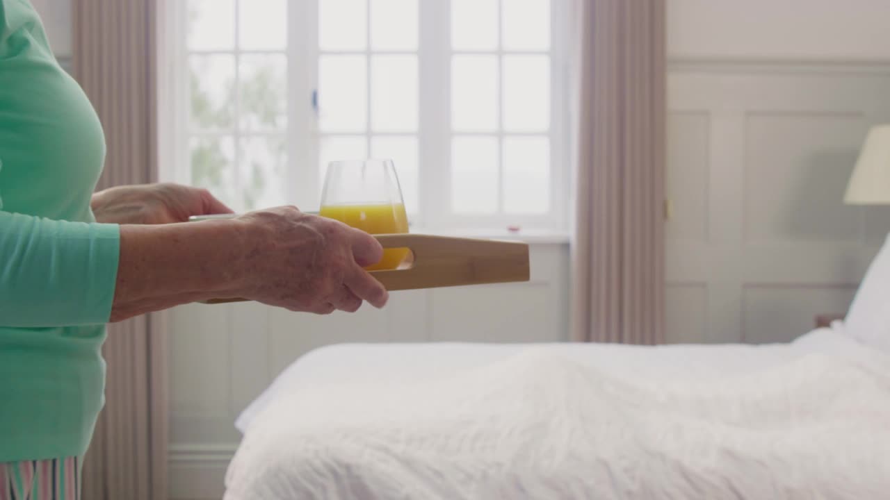 老年夫妇在家里，女人把早餐放在托盘上送到老年男子的床上视频素材