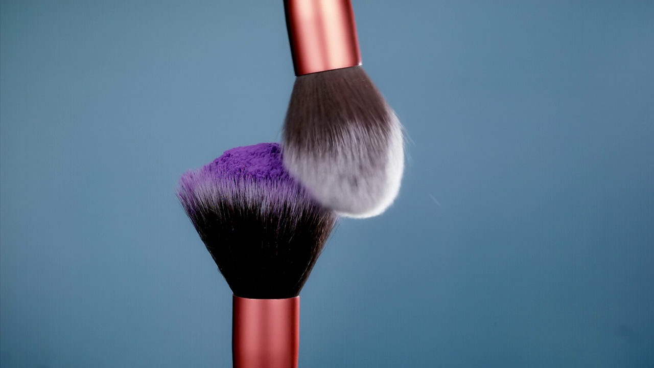 化妆刷与紫色粉末爆炸在蓝色背景超级慢动作视频素材