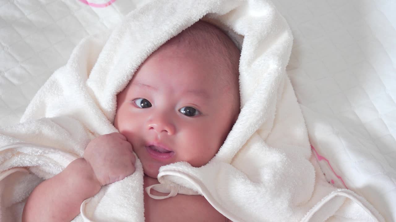 可爱的亚洲新生儿躺在床上白色的毯子在卧室。小男孩看着镜头，笑着开心的脸。天真的小婴儿，刚出生的第一天。母亲一天的概念。视频下载