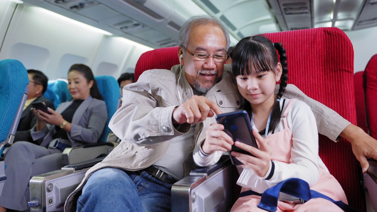 亚洲的老爷爷和他的侄女喜欢在飞机上一起用智能手机看电影，共享耳机视频下载