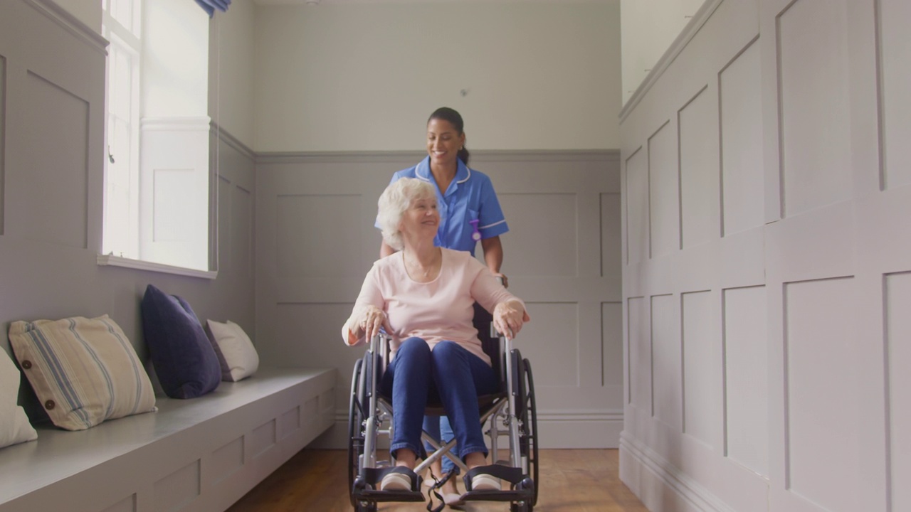 老年妇女在家被穿着制服的女护理人员推着轮椅的肖像视频素材