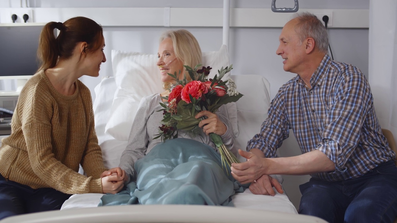 快乐的老丈夫和年轻的女儿来访，快乐的女人躺在医院病房的床上视频下载