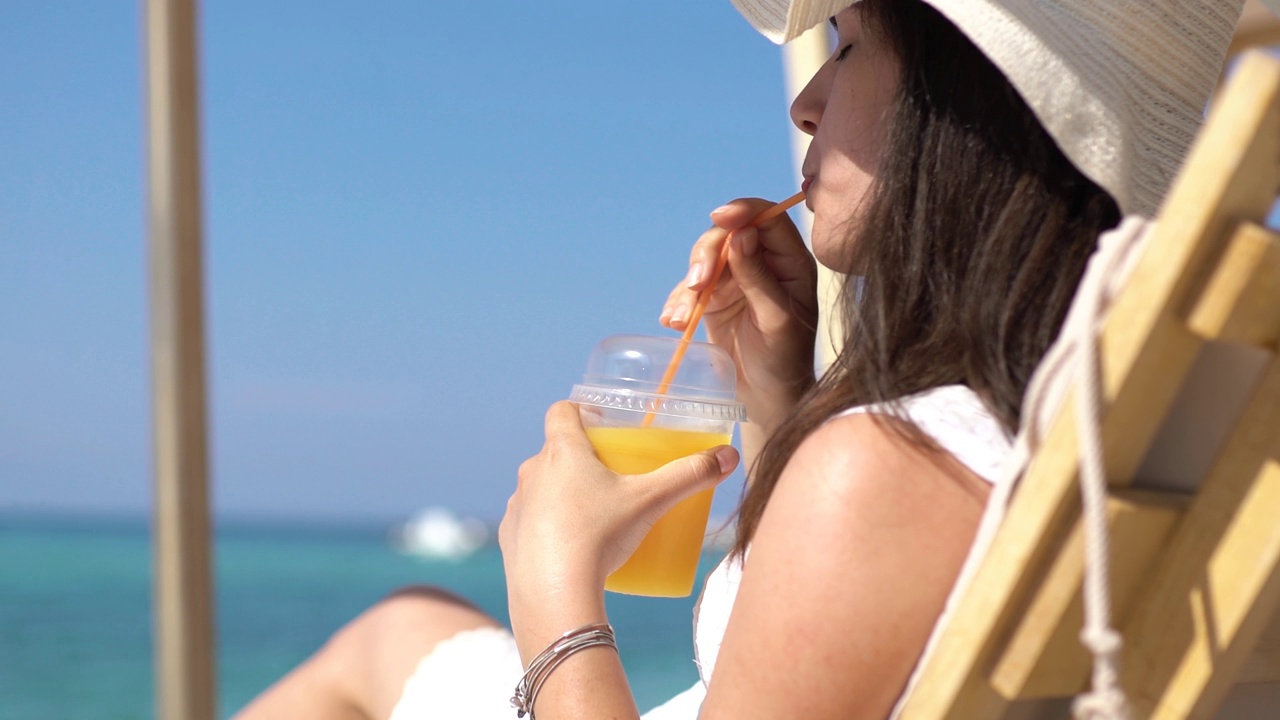 年轻女子在海滩上享受橙汁视频素材