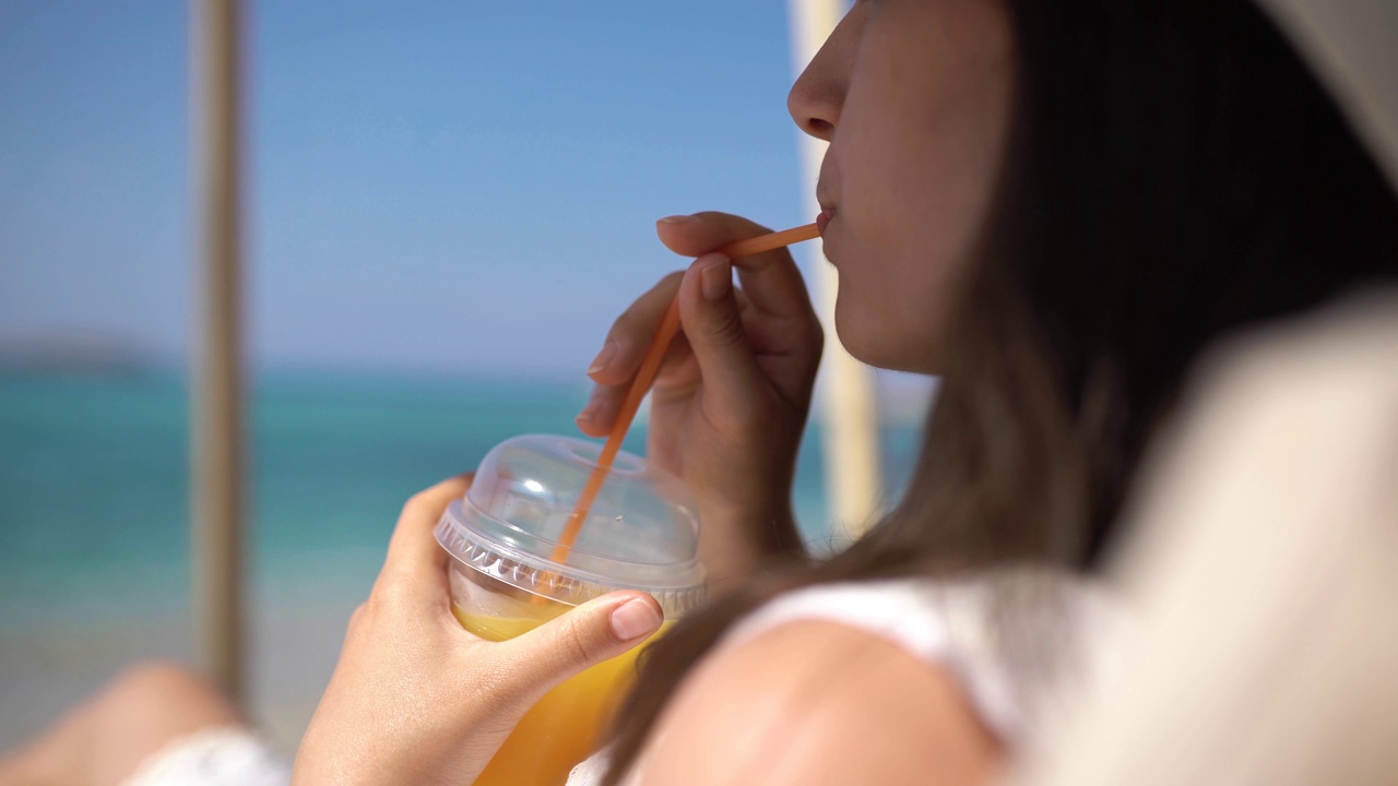 年轻女子在海滩上享受橙汁视频素材