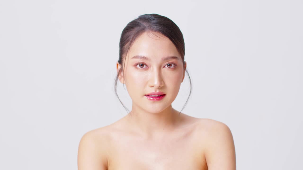 美丽的亚洲女人看着镜头微笑手与清洁和新鲜的皮肤幸福和快乐积极的情绪，孤立在白色的背景，美容和化妆品的概念视频下载