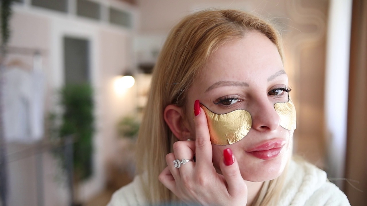 年轻女子正在涂金色的胶原蛋白眼罩视频素材