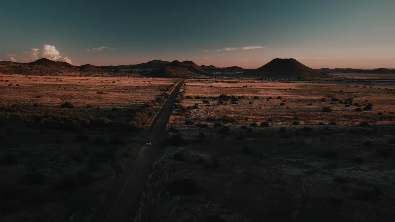 广角无人机拍摄日落时分一辆4x4在土路上行驶的视频，南非自由州视频下载