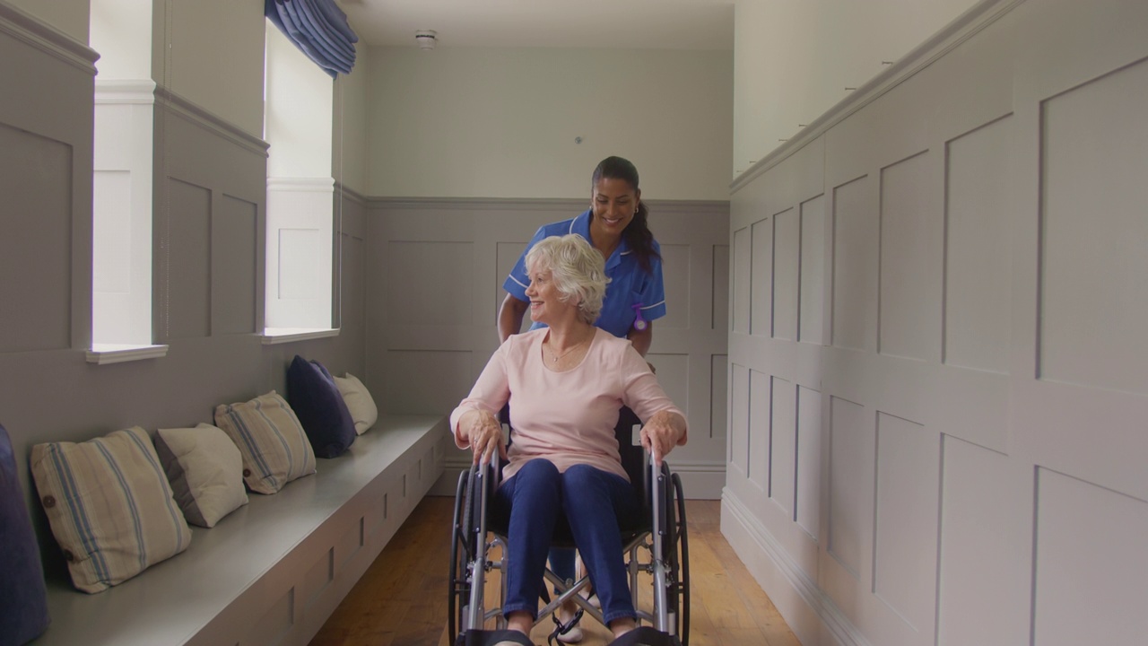 在家里，被穿着制服的女护理人员推着轮椅的老年妇女视频素材