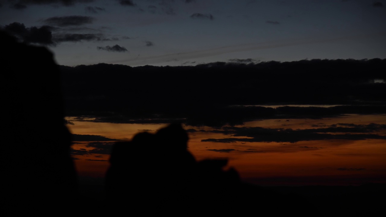 时间的推移，黄昏变成黑夜。落日的云彩，前景是一块岩石的剪影视频素材