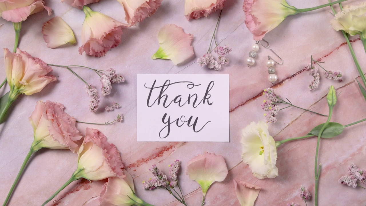 一张大理石桌子上的感谢卡片，旁边是粉红色的花朵。俯视图放大视频下载