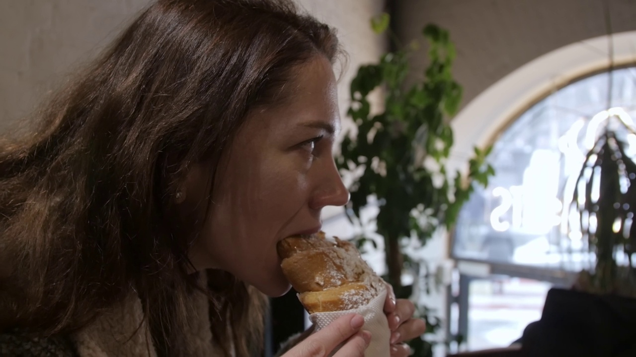 年轻女子在咖啡馆里吃着美味的烤牛角面包。视频素材