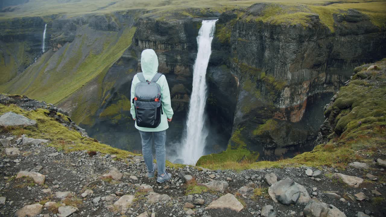 在冰岛高地上，一名女子背着背包欣赏海弗斯瀑布视频素材
