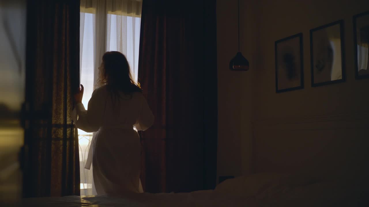 清晨，女人打开窗帘从大窗户欣赏景色视频下载