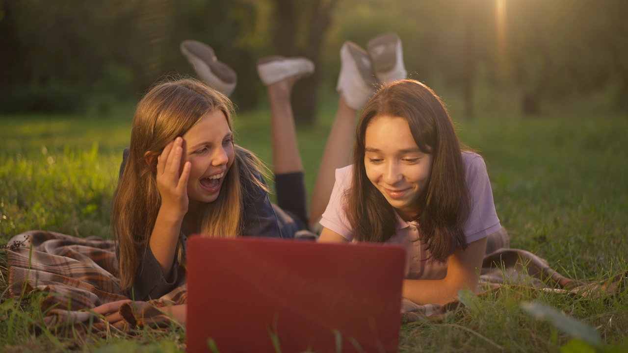 两个笑着的少女躺在夏日春天公园的阳光下，在社交媒体上讨论谣言。前视人像放松悠闲的高加索朋友享受周末日落。视频下载