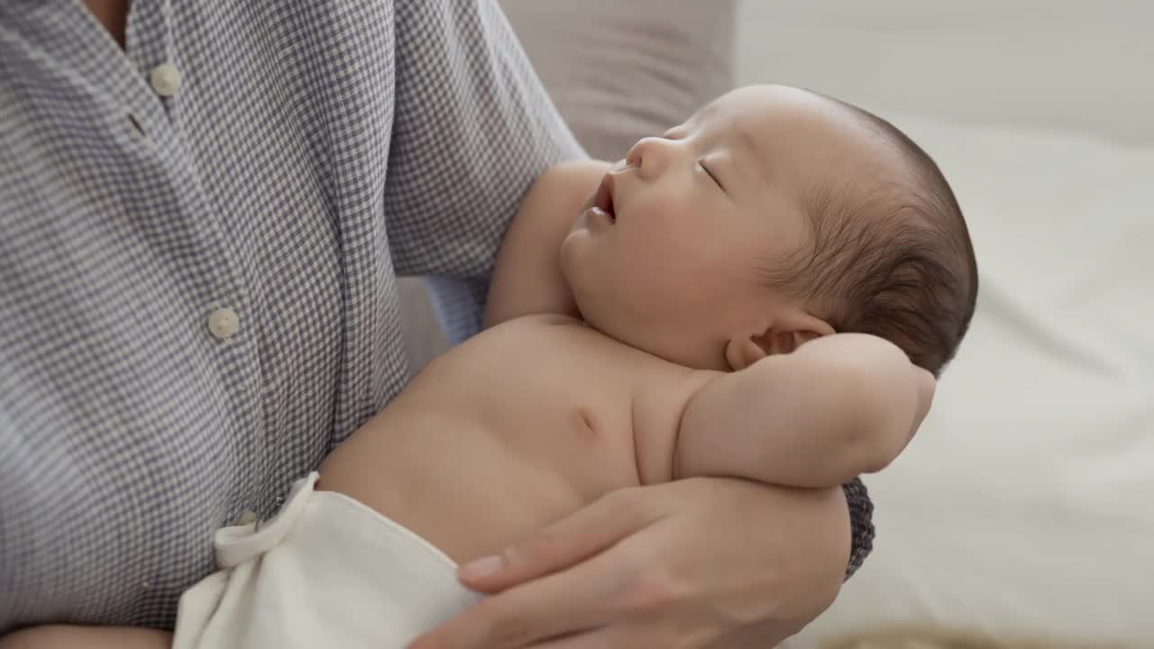 4k，一个两个月大的亚洲新生儿的特写，脱光衣服躺在母亲的腿上。有一位母亲，她悉心照料视频素材