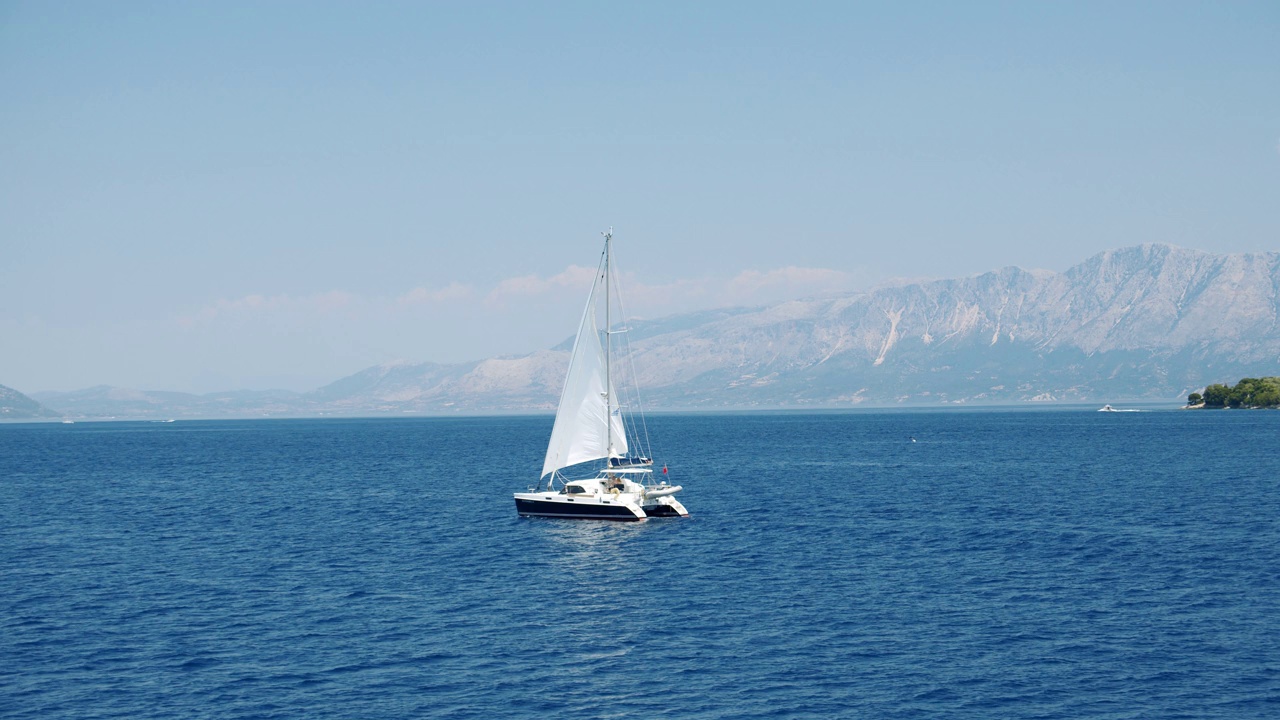 双体游艇航行在开阔的蓝色海洋。海岸线在bachground视频下载