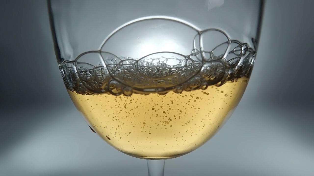 创意宏慢动作4k视频白葡萄酒倒入杯子。玻璃与倒白葡萄酒与飞溅和泡沫的特写。视频素材