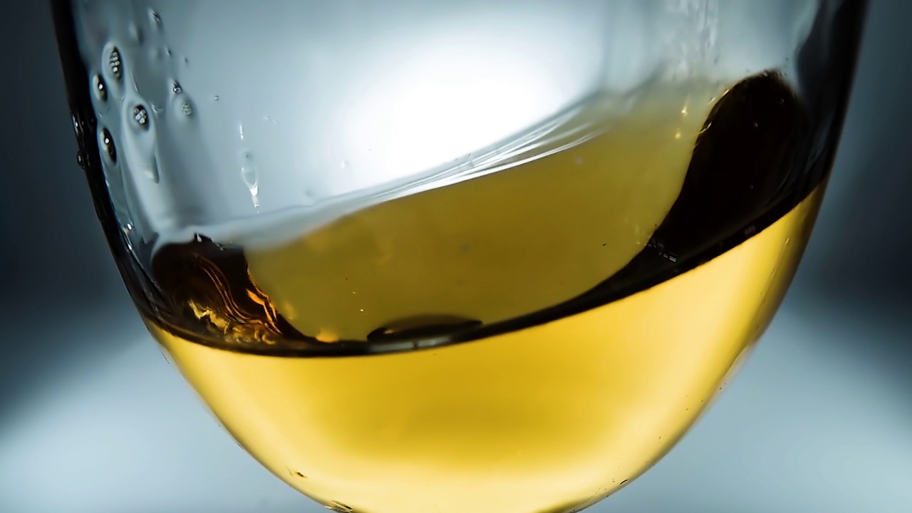 创意微距慢动作4k视频白葡萄酒溅在杯子从一边到另一边像波浪。酒杯溅酒特写。视频素材
