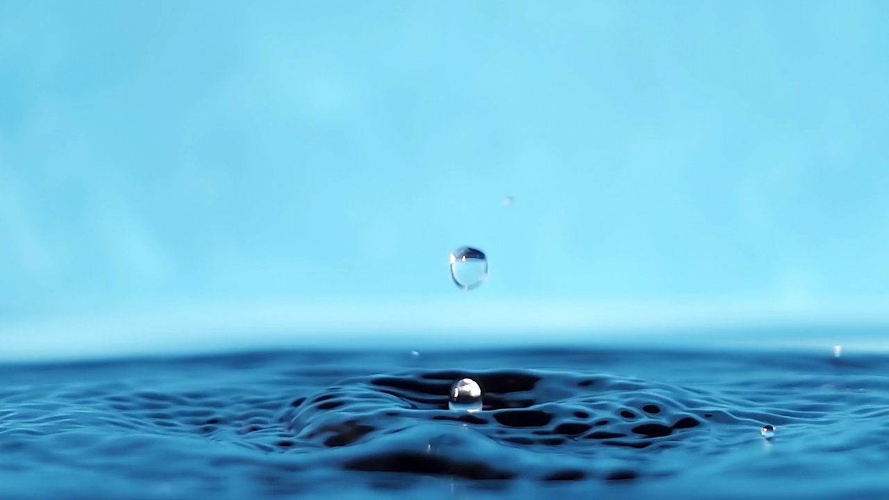 慢动作4k视频水面与下落的水滴在蓝色背景。泼水。工作室拍摄。视频下载
